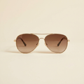 Capucine classic aviator sunglasses in gold metal with brown gradient lenses, against a cream studio backdrop
