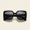 Celeste oversized square sunglasses in glossy black with dark grey lenses, against a cream studio backdrop