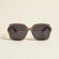 Fleur oversized polarised sunglasses in taupe grey with smoke lenses, against a cream studio backdrop
