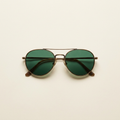 Ines retro aviator sunglasses in antique bronze with green lenses, against a cream studio backdrop