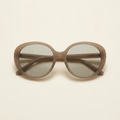 Noemie oversized rounded sunglasses in greige taupe with smoke lenses, against a cream studio backdrop